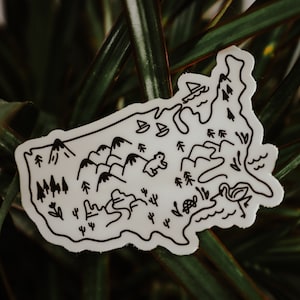 May include: A white sticker with a black outline of the United States. The sticker features various illustrations of nature, including mountains, trees, a bear, a turtle, a flamingo, and a sailboat.