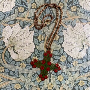 May include: A gold chain necklace with a green and red enamel cross pendant featuring floral details. The pendant is shaped like a cross with red flowers and green leaves.
