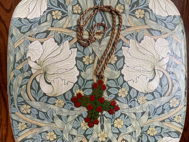 May include: A gold chain necklace with a green and red enamel cross pendant featuring floral details. The pendant is shaped like a cross with red flowers and green leaves.