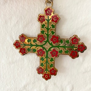 May include: A gold-toned cross pendant with red and green enamel detailing. The cross is decorated with a floral design featuring red flowers and green leaves.