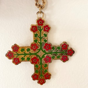 May include: A gold chain necklace with a cross pendant. The cross is decorated with red and green enamel flowers.