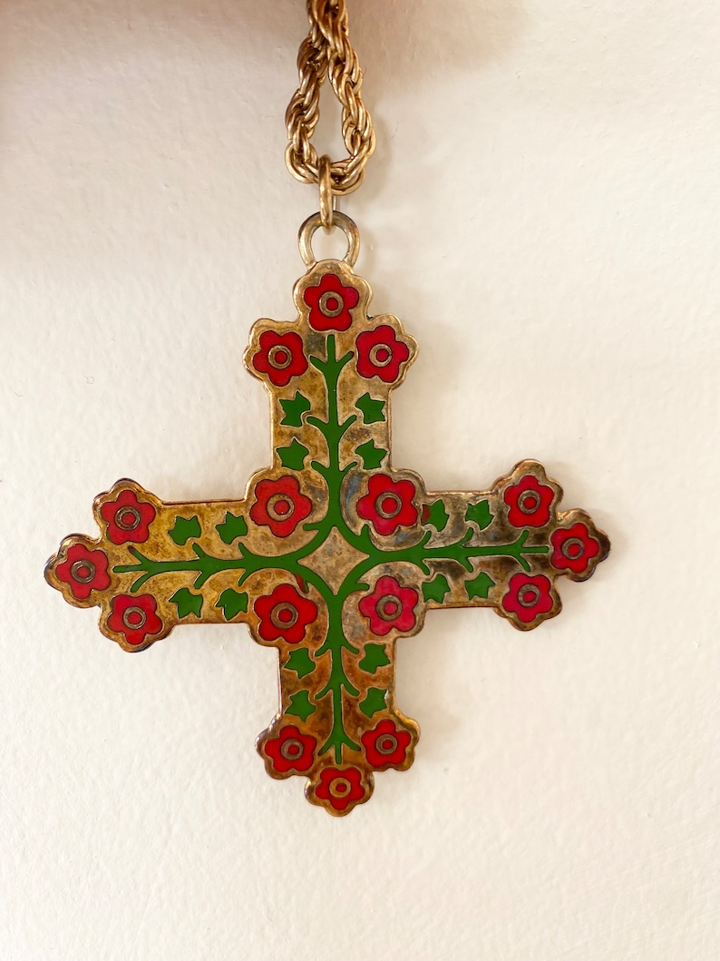 May include: A gold chain necklace with a cross pendant. The cross is decorated with red and green enamel flowers.