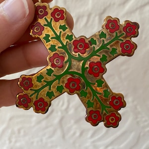 May include: A gold-toned metal cross pendant with a floral design. The cross is decorated with red and green enamel, featuring stylized flowers and leaves.