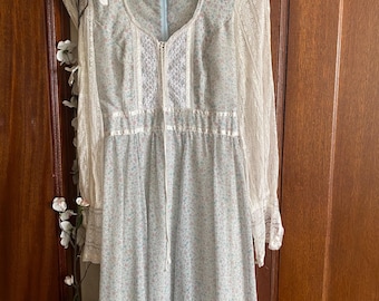 May include: A floor-length dress featuring a light blue and pink floral print on a white background. The garment has long, sheer lace sleeves, a scoop neckline with a central lace panel, and a light blue zipper closure at the upper back.