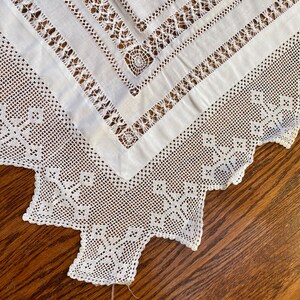 May include: White crocheted tablecloth with a square design in the centre and a scalloped edge. The tablecloth is on a wooden surface. The tag says "Crochet, 42" x 32", &pound;25.00"