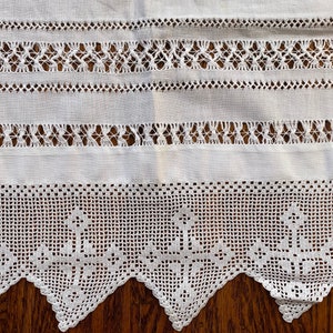 May include: White crocheted lace trim with a scalloped edge. The lace has a delicate pattern and is perfect for adding a touch of elegance to any project.