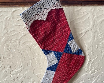 May include: A red, white, and blue patchwork Christmas stocking with a white crocheted trim. The stocking is quilted and has a blue and white geometric pattern.