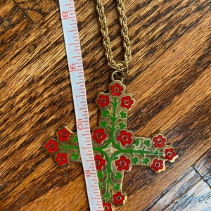 May include: A gold chain necklace with a large cross pendant. The cross is decorated with red and green enamel flowers.