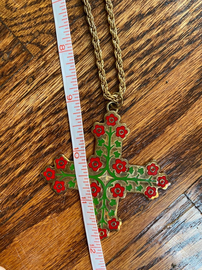 May include: A gold chain necklace with a large cross pendant. The cross is decorated with red and green enamel flowers.