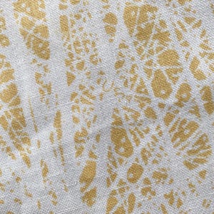 Könnte beinhalten: Nahaufnahme eines weißen Stoffes mit einem sich wiederholenden Muster aus goldgelben organischen Formen. Das Design hat ein strukturiertes Aussehen, wobei die gelben Formen abstrakten floralen oder blattartigen Formen ähneln. Der Stoff hat eine subtile, gewebte Textur.