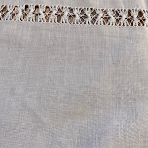 May include: A close-up of a white linen fabric with a delicate lace trim. The fabric has a subtle texture and a slightly off-white hue.