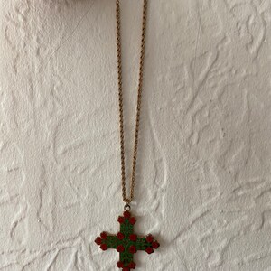 May include: A gold chain necklace with a large cross pendant. The cross is decorated with red and green enamel and features a floral design.