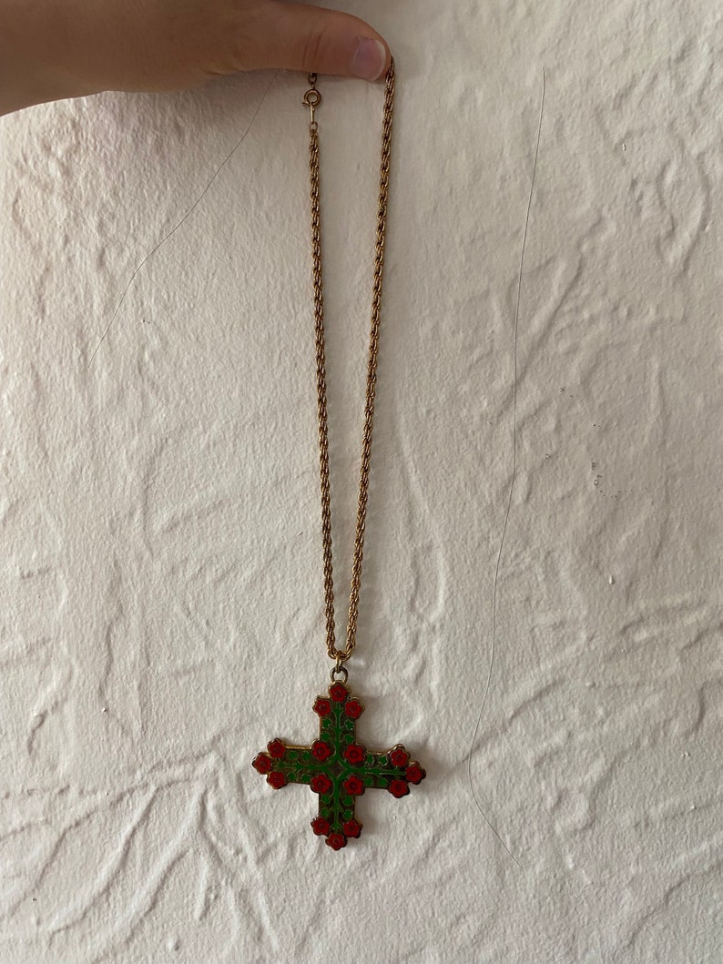 May include: A gold chain necklace with a large cross pendant. The cross is decorated with red and green enamel and features a floral design.