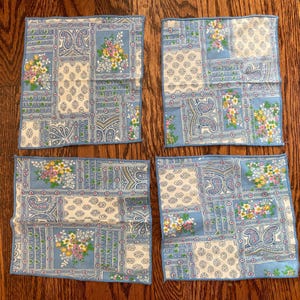 Puede incluir: Cuatro pañuelos de color azul claro y crema con un diseño de patchwork floral y paisley. Cada pañuelo presenta un borde azul y un patrón repetido de flores y elementos decorativos.