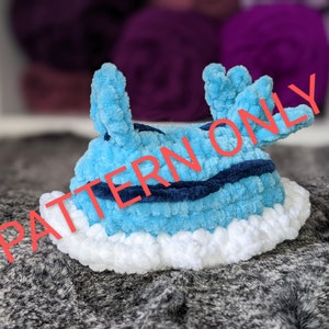 May include: A blue and white crocheted sea slug with a blue and white striped pattern. The sea slug is sitting on a gray surface.
