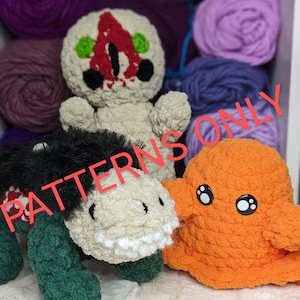 May include: Three crocheted plush toys: a white and red creature with green eyes, a green and white creature with black fur, and an orange creature with black eyes. The toys are sitting on a white surface. PATTERNS ONLY.