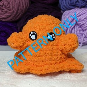 Puede incluir: Un juguete de peluche de pulpo naranja tejido a crochet con ojos blancos y huellas de patas negras. El juguete está sentado sobre una superficie blanca y esponjosa.