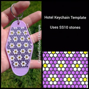 Pode incluir: Modelo de chaveiro de hotel roxo com um exemplo de produto finalizado. O chaveiro é decorado com strass brancos e roxos em um padrão de flores. O texto "Andrea's Custom Crafts" e "Finished Product Example" é visível no chaveiro. O modelo usa pedras SS10.