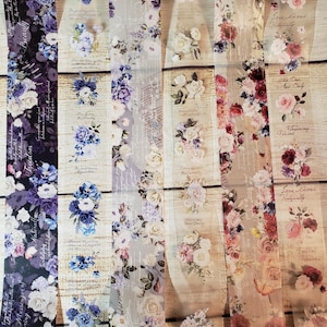 May include: Five rolls of decorative washi tape featuring floral patterns and text. The tape is transparent with a white background. The floral patterns include roses, peonies, and other flowers in shades of pink, purple, and blue. The text on the tape includes quotes about love, beauty, and nature.