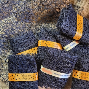 May include: Dark blue decorative mesh rolls, perfect for Halloween crafts. Each roll is wrapped with orange ribbon printed with "Trick or Treat!" and "Pumpkin Carving" in a playful font. The mesh has a web-like appearance.