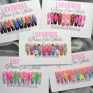 May include: Five sets of press-on nails displayed on white cards labeled LUXURIOUS Press On Nails ExtravaNova. The nails feature various designs including 3D flowers, animal prints, rhinestones, and vibrant colors like pink, green, and blue.