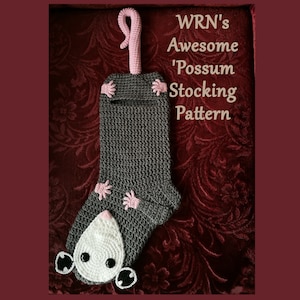 May include: A gray crocheted Christmas stocking shaped like a possum with a pink tail. The stocking has a white face with black eyes and a pink nose. The text "WRN's Awesome 'Possum Stocking Pattern" is written in brown text above the stocking.