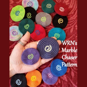 May include: A collection of colourful crocheted coasters with a swirling pattern. The coasters are arranged in a circle on a red surface. The text "WRN's Marble Chaser Pattern" is visible in the image.