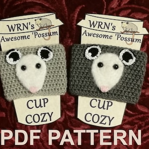 May include: Two grey crocheted cup cozies with a possum face design. The cozies are labelled "WRN's Awesome 'Possum Cup Cozy" and "PDF Pattern".