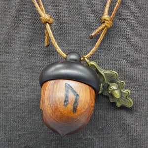 May include: A wooden acorn pendant necklace with a brown leather cord and a small metal acorn charm. The acorn is carved with a rune symbol.