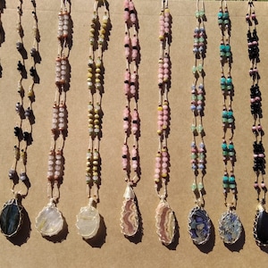 May include: Ten necklaces with wire-wrapped gemstone pendants. Each necklace features a different gemstone, including labradorite, quartz, tiger's eye, rose quartz, amethyst, turquoise, black onyx, and jasper. The necklaces are made with various beads and have a natural, earthy aesthetic.