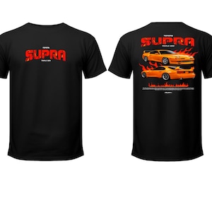May include: Black t-shirt featuring the text "TOYOTA SUPRA TRIPLE GEN" in red flame-style font on the front. The back of the shirt displays two orange Toyota Supra cars with flames, and the text "TOYOTA SUPRA TRIPLE GEN".