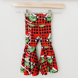 May include: Red and black plaid bell bottom pants with a green Grinch print. The pants have a festive Christmas theme.
