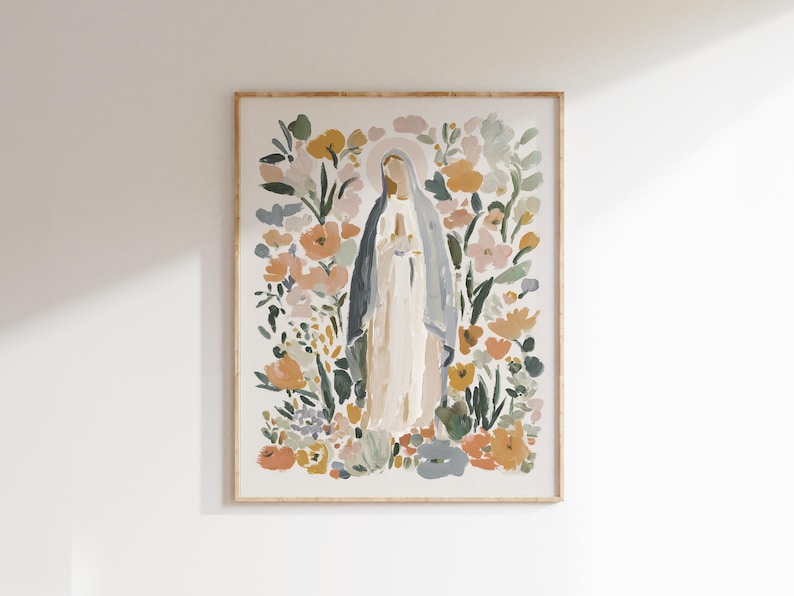 May include: A framed art print featuring a watercolor painting of a religious figure surrounded by colorful flowers. The figure is depicted in a white robe and blue veil, with a halo. The floral arrangement includes shades of orange, yellow, and green.