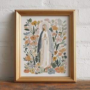 May include: A framed art print featuring a watercolor painting of a religious figure surrounded by flowers. The figure is depicted in a white robe and blue veil, with a halo. The floral arrangement includes peach, yellow, and green hues. The frame is gold.