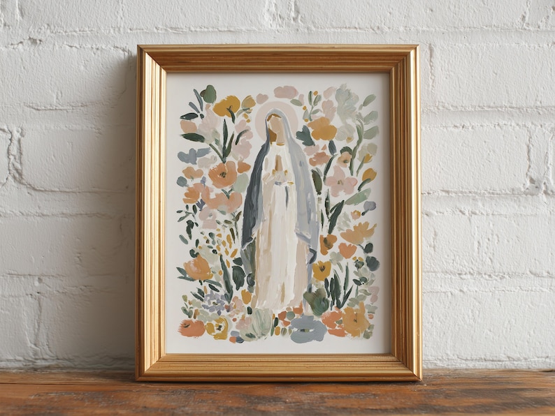 May include: A framed art print featuring a watercolor painting of a religious figure surrounded by flowers. The figure is depicted in a white robe and blue veil, with a halo. The floral arrangement includes peach, yellow, and green hues. The frame is gold.