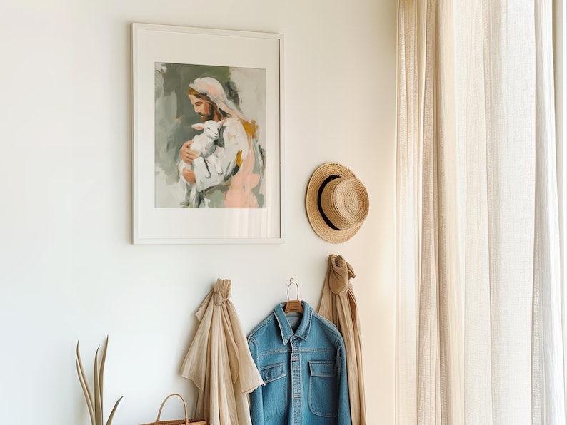 Peut inclure: Une &oelig;uvre encadr&eacute;e repr&eacute;sente une figure tenant un agneau, dans des couleurs douces. Un chapeau de paille et une veste en jean sont accroch&eacute;s au mur. Une &eacute;charpe beige et un sac fourre-tout tiss&eacute; sont &eacute;galement visibles.