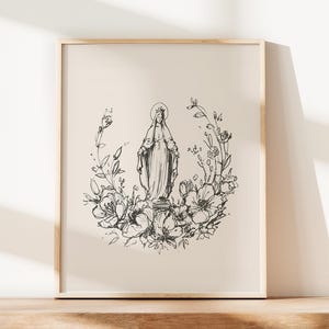 Puede incluir: Impresión artística enmarcada que presenta un boceto en blanco y negro de una figura religiosa, rodeada por una corona floral. La obra de arte se muestra en un marco de madera de color claro, para la decoración del hogar.