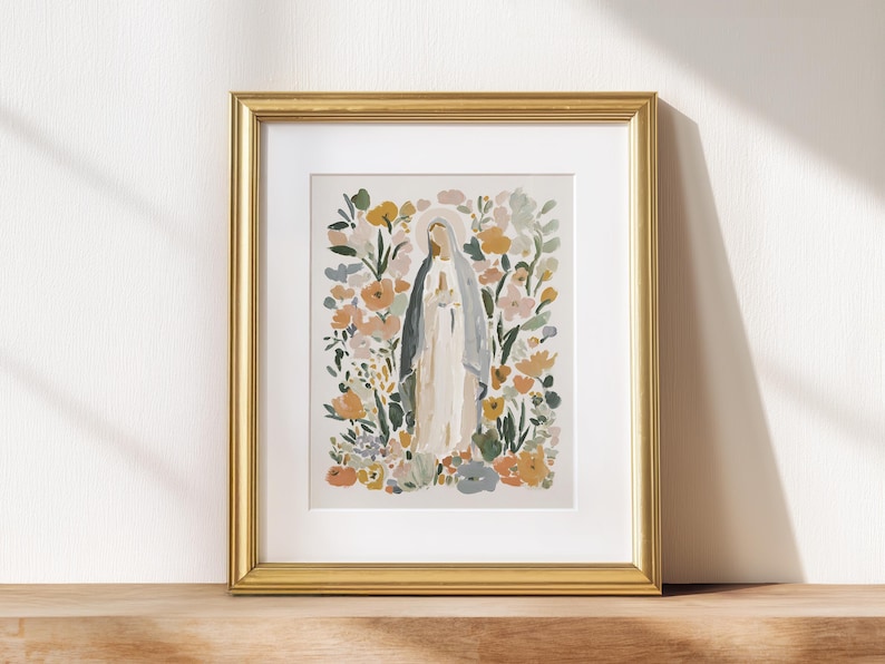 May include: A framed art print featuring a watercolor illustration of a religious figure surrounded by colorful flowers. The artwork is set in a gold frame and displayed on a wooden surface, creating a serene and decorative piece.