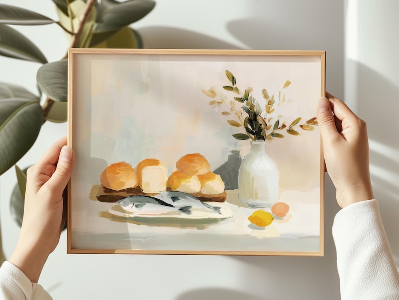May include: A framed art print depicting a still life scene. The painting features a plate with fish, bread rolls, a vase with greenery, and a lemon. The color palette includes beige, white, and shades of orange and green.