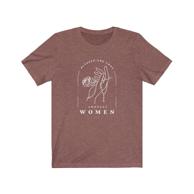Peut inclure: Un t-shirt marron chin&eacute; avec un motif blanc repr&eacute;sentant une main tenant un chapelet et une rose. Le texte "Blessed are thou amongst women" est imprim&eacute; sous le motif.