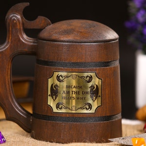 Könnte beinhalten: Ein dunkelbrauner Bierkrug aus Holz mit Deckel und Griff. Der Krug hat ein Messingschild mit dem Text "BECAUSE I AM THE DM THAT'S WHY" und Drachenillustrationen. Der Griff hat einen Flaschenöffner.