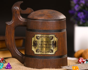 May include: A dark brown wooden beer stein with a lid and handle. The stein features a brass plaque with the text "BECAUSE I AM THE DM THAT'S WHY" and dragon illustrations. The handle has a bottle opener.