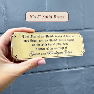 May include: A 15cm x 5cm solid brass plaque with decorative edges. The plaque has engraved text that reads: "This Flag of the United States of America was flown over the United States Capitol on the 24th day of May 2025 in honor of the marriage of Garrit and Brooklynn Geiger."