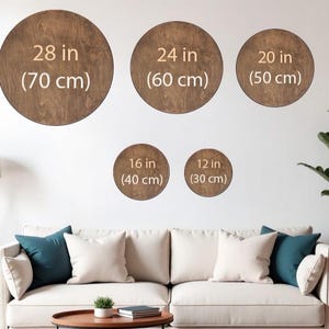 May include: A display of five wooden, circular wall art pieces in varying sizes: 28 in (70 cm), 24 in (60 cm), 20 in (50 cm), 16 in (40 cm), and 12 in (30 cm). The brown circles are mounted on a white wall above a sofa with pillows.