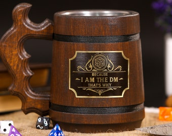 May include: Wooden beer mug with a dark brown finish and a decorative handle. The mug features a metal interior and a gold-colored plaque with the text "BECAUSE I AM THE DM THAT'S WHY". Dice are visible in the foreground.