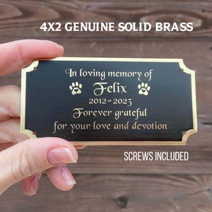 May include: A 4x2 inch solid brass memorial plaque with a black surface and gold trim. The plaque reads "In loving memory of Felix" with paw prints, dates, and a heartfelt message. The text "SCREWS INCLUDED" is also visible.