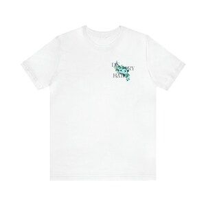 May include: White t-shirt with a floral design and the text "Discovery Hat" printed on the front.