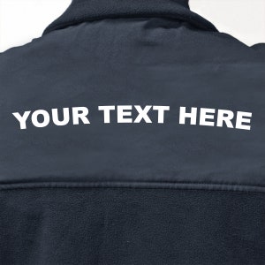 以下が含まれることがあります： 背面に白い文字で「YOUR TEXT HERE」と印刷された濃い青色のフリースジャケットです。