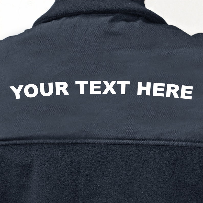 以下が含まれることがあります： 背面に白い文字で「YOUR TEXT HERE」と印刷された濃い青色のフリースジャケットです。