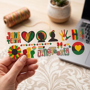 May include: A clear sticker sheet featuring various Juneteenth-themed graphics. Designs include the words "June Teenth," hearts, silhouettes, a sunflower, raised fists, a bow, and a circle with a heart. The color palette includes red, yellow, green, and black.